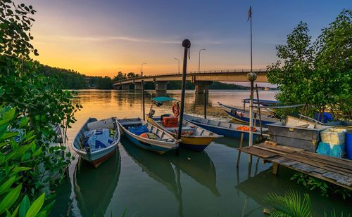 Boats moored in river against sky at sunset