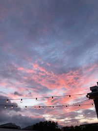 Low angle view of illuminated light bulbs against dramatic sky during sunset