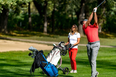 Golfing couple at a tee box, enjoying a game of golf on a beautiful sunny day, man hitting a ball