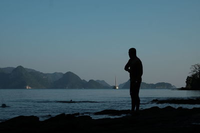 Silhouette man standing on sea against clear sky