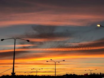 Low angle view of street lights against orange sky