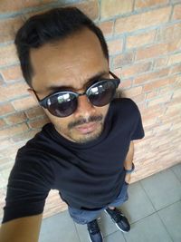 Portrait of man wearing sunglasses standing against brick wall