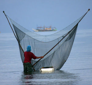 Rear view of man fishing in sea against sky