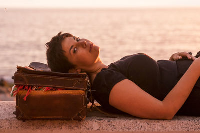 Portrait of woman lying down on retaining wall against sea