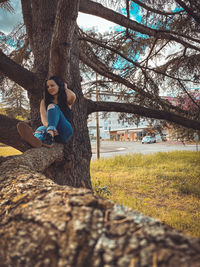 Full length of young woman sitting on tree trunk