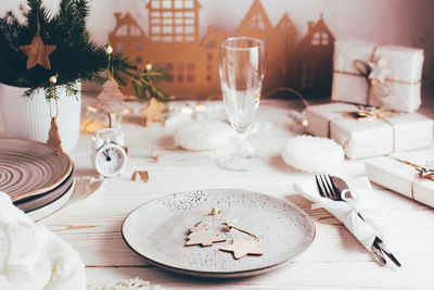 Plate with wooden decorations, cutlery, champagne glass and cardboard house