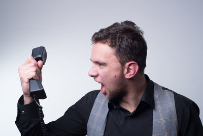 Young businessman shouting at landline phone against gray background