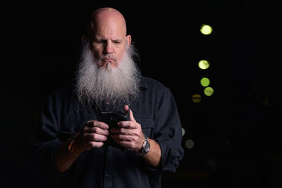 Man using mobile phone while standing against black background