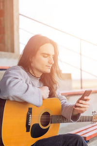 Close-up of young man holding guitar while using mobile phone