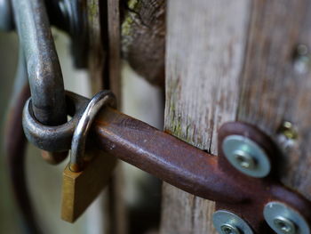 Close-up of padlock on rusty latch of wooden door