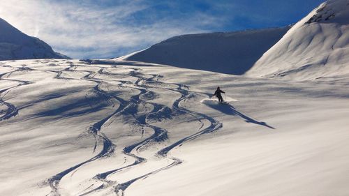 Rear view of person skiing on snow covered mountain against blue sky