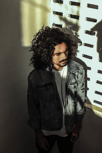 Young man looking away while standing against wall