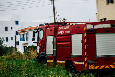 Red bus on field by buildings against sky