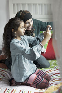 Mother and daughter photographing in bedroom