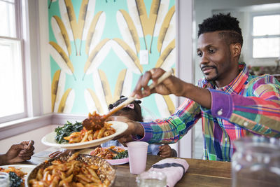 Man serving food in plate while having meal with family at home