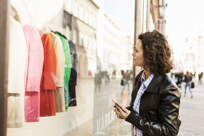 Businesswoman doing window shopping while holding mobile phone in city