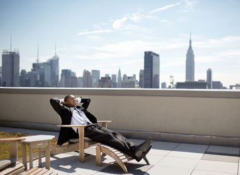 Businessman relaxing on lounge chair against sky