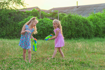 Two little girls play in the summer on a green meadow with water pistols