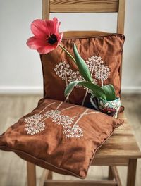 Pink tulip in vintage vase on wooden chair with brown embroidered cushions.