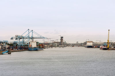 Cranes at harbor against sky