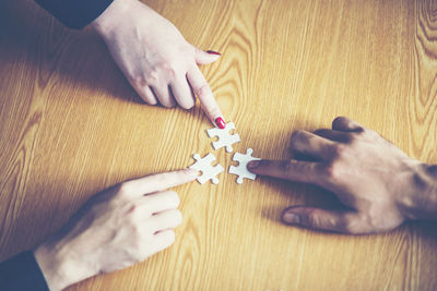 Cropped hands of business colleagues playing jigsaw puzzle at desk in office