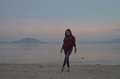 Rear view of woman standing at beach against sky during sunset