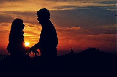 Silhouette of people standing on mountain at sunset