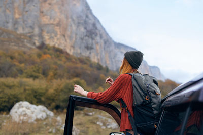 Rear view of woman sitting on mountain against sky