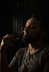 Portrait of man smoking pipe in darkroom 