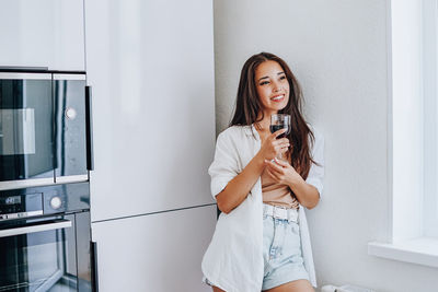 Portrait of smiling young woman standing against wall