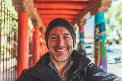 Man dressed in warm clothing smiles at camera in foreground against dynamic orange red breezeway