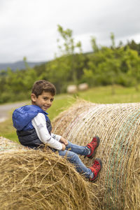 Portrait of cute boy sitting on hay bale