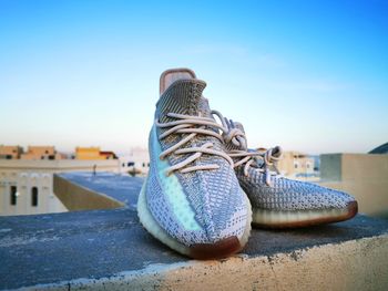 Close-up of shoes on retaining wall against blue sky