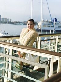 Portrait of smiling woman standing by railing on pier