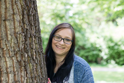 Portrait of smiling mid adult woman standing by tree at park
