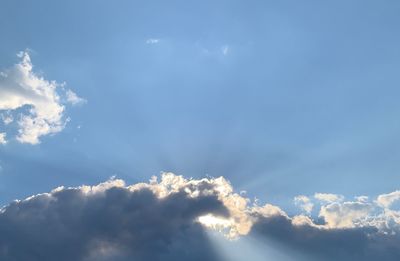 Low angle view of sunlight streaming through clouds