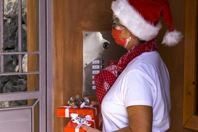Senior woman wearing mask holding gift standing by door