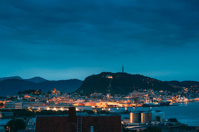 Illuminated city by sea against sky at dusk