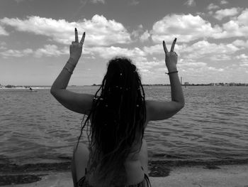 Rear view of woman gesturing peace sign while sitting against sea at beach