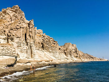 Rock formations by sea against clear blue sky