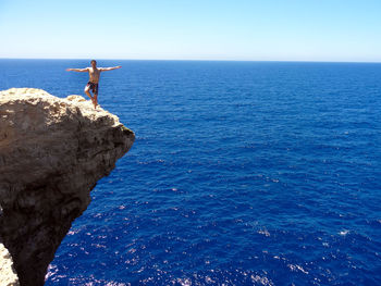 Shirtless man standing on cliff by sea