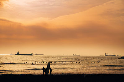 Silhouette people on beach against sky during sunset