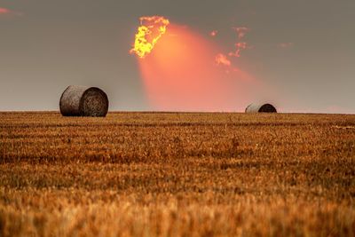 Hay bales on field against sky during sunset