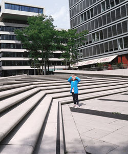 Rear view of man walking on footpath amidst buildings in city