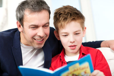 Close-up of smiling father and son reading book at home