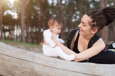 Smiling woman looking at cute daughter by tree trunk