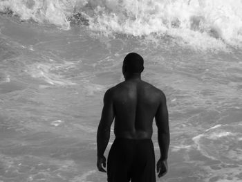 Rear view of shirtless man standing by sea