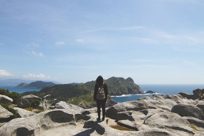 Rear view of woman standing on rock against sky