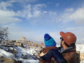 Father with child looking at birds in sky during winter