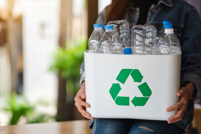 A woman collecting and holding a recyclable garbage plastic bottles in a trash bin at home